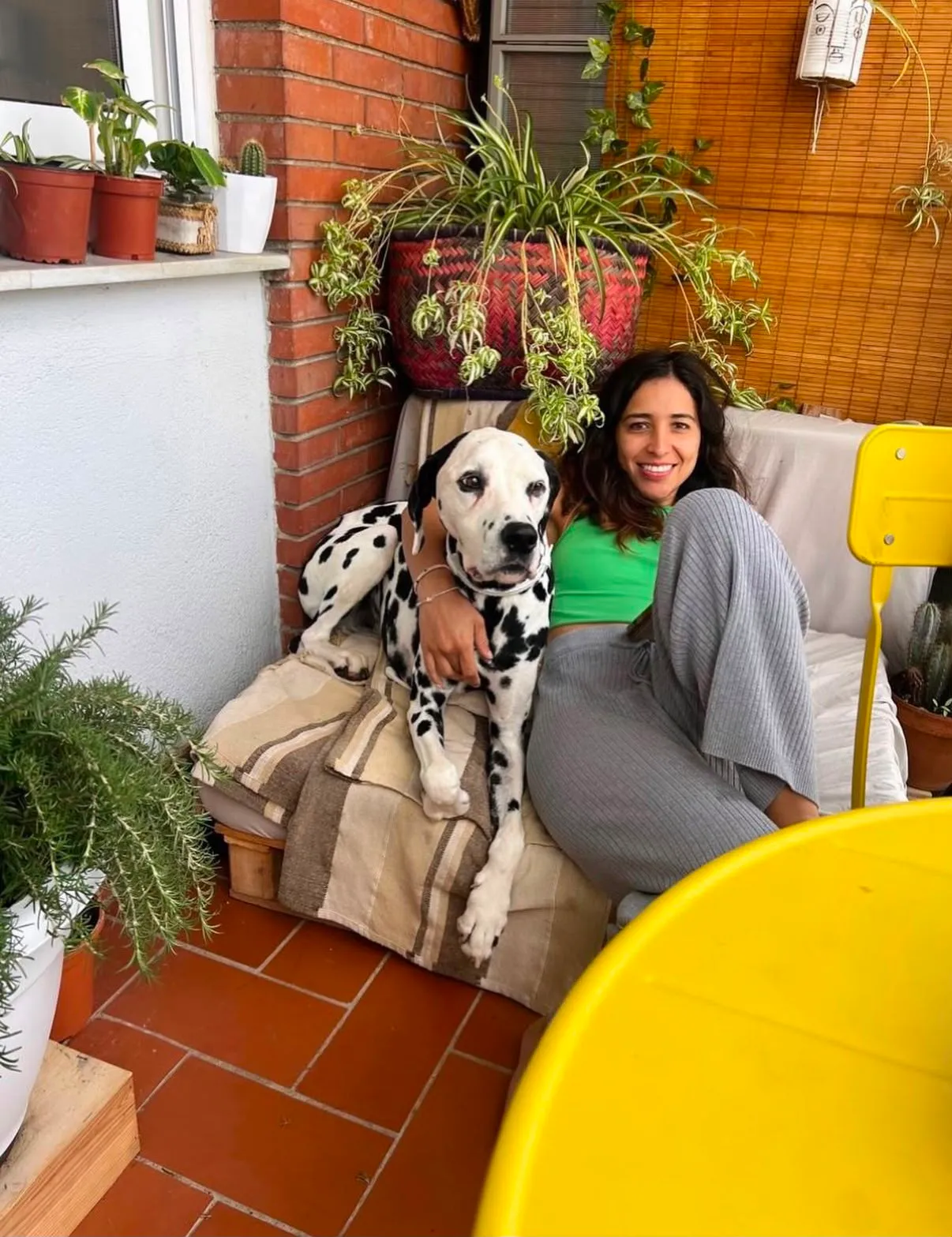 Mariana y un dálmata relajados en una terraza llena de plantas, como en casa, durante el hospedaje en Barcelona