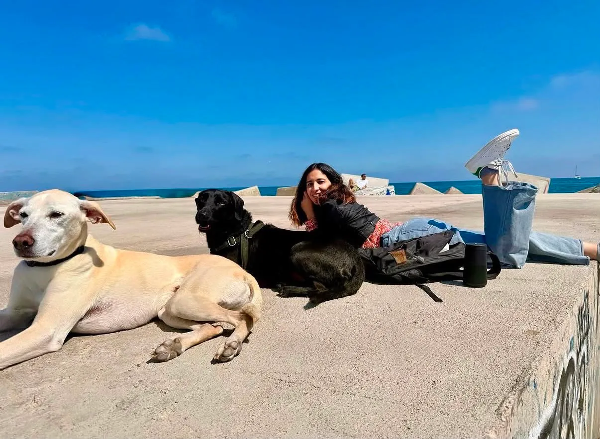 Mariana, cuidadora de Marcando Huella, descansando en la playa de Barcelona junto a dos perros tranquilos y felices