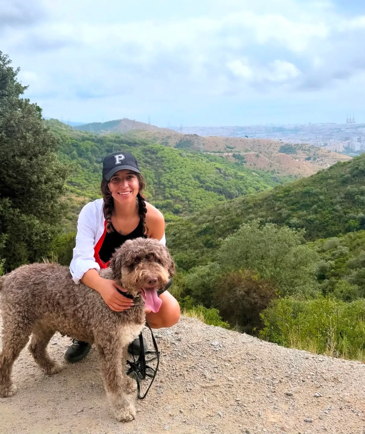 Mariana abrazando a un perro de agua en las colinas de Collserola con Barcelona al fondo